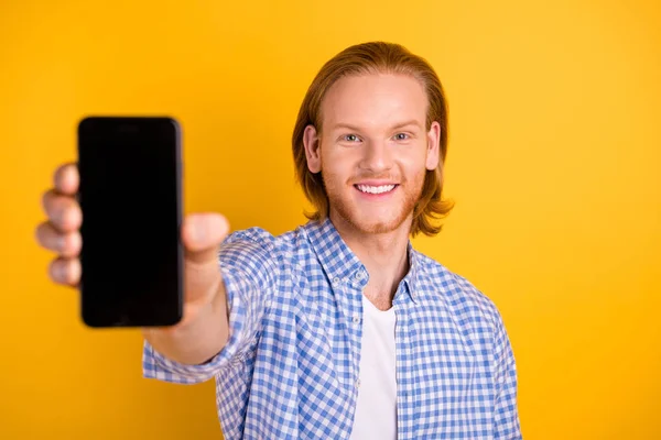 陽気なハンサムなプロモーターの写真は、鮮やかな色の背景の上に隔離チェッカーブルーのシャツを着て歯ごたえで微笑む電話の新しいモデルを提示 — ストック写真