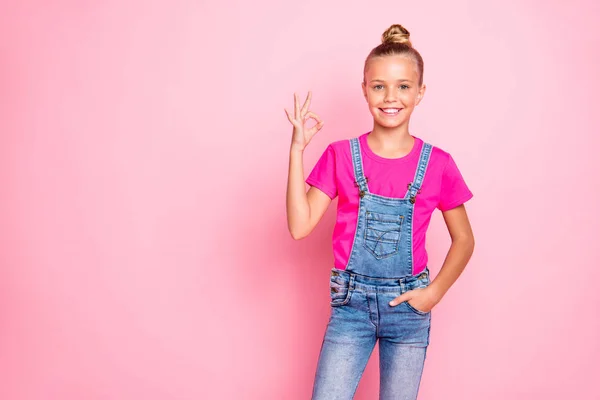 Foto de alegre linda linda niña preadolescente que muestra que ok signo de aprobación de sus acciones de la mano en el bolsillo de los pantalones vaqueros en general aislado sobre fondo de color pastel rosa —  Fotos de Stock