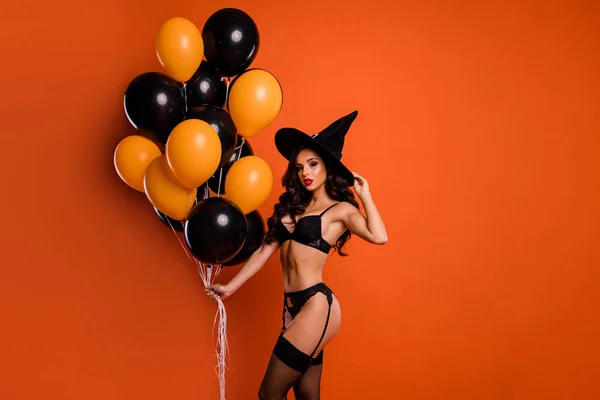 Bild av vacker naken charmig dam röda läppar hålla luft ballonger retas stilig trollkarl visar perfekt passform former bära bikini tights häxa mössa isolerad orange bakgrund trick eller behandla — Stockfoto