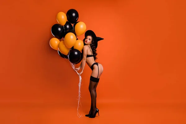 Full storlek foto av vackra naken dam hålla luft ballonger gör privat fest visar make idealisk figur bära svart bikini tights häxa mössa isolerad orange bakgrund — Stockfoto