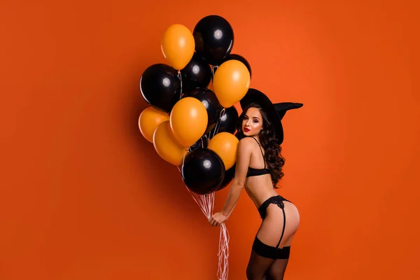 Profilo foto di bella signora nuda tenere i palloncini d'aria pronti per la festa privata con ragazzo che mostra forme perfette indossare collant bikini cappello strega isolato sfondo arancione — Foto Stock