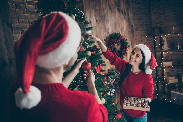 ロマンチックな女性の裏側の肖像画は、彼女の夫を見て常緑のクリスマスツリーを飾るボーブルのコレクションを保持し、屋内で新年の照明と家の中でX-masの準備を楽しむ — ストック写真