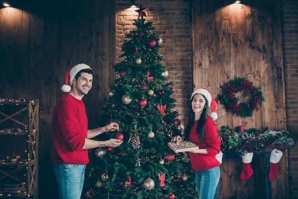 Portrait of nice attractive lovely positive cheerful cheery married spouses spending chistmastime custom putting balls toys on fir in decorated loft industrial brick wood style interior — 스톡 사진
