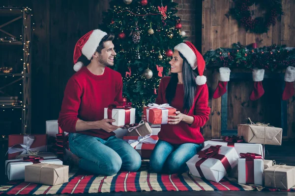 Foto lateral de perfil de tamaño completo de dos personas casadas románticas en sombrero de gorra dan paquetes en tiempo de Navidad sentarse en manta a cuadros en casa con decoración de año nuevo en el interior —  Fotos de Stock