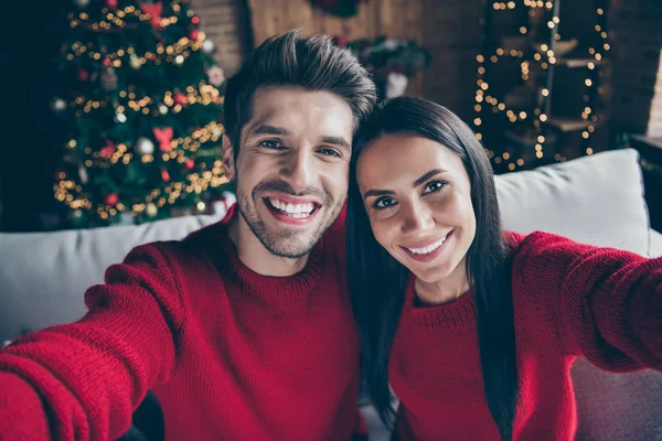 Foto de cerca de dos personas novios románticos en pullovers rojos haciendo selfie en x-mas vacaciones de Navidad sentarse en diván interior lleno de iluminación luces de año nuevo — Foto de Stock