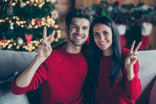 Çekici, evli iki romantik insanın portresi V-işaretleri yaptırıyor. Yeni yıl Noel 'i kutluyorlar. Evdeki divanda oturuyorlar. — Stok fotoğraf