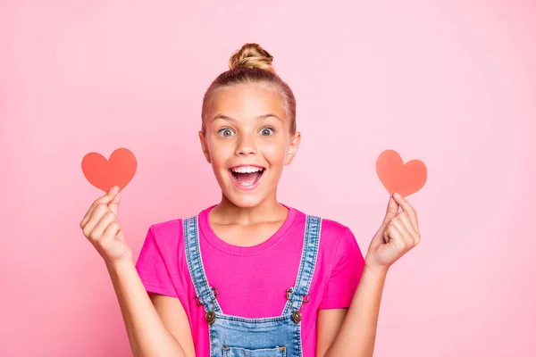 Foto de animado alegre bonito agradável estudante segurando dois ouvir formas vermelhas com as mãos vestindo jeans jeans geral fuchsia t-shirt isolado sobre cor pastel rosa fundo — Fotografia de Stock