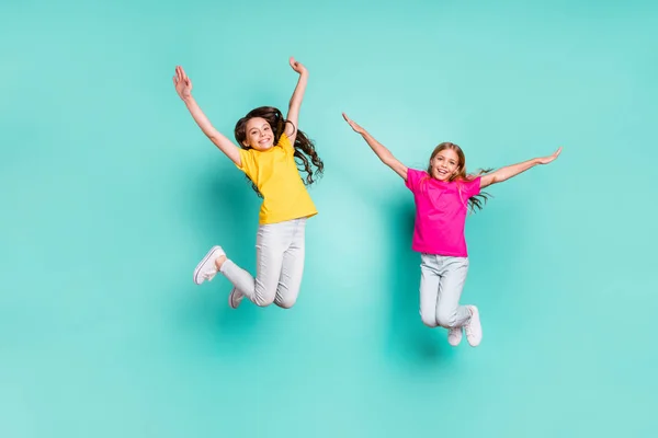 Full length body size photo of two enjoying girls being free wearing yellow and pink t-shirts while isolated with teal background — Stock Photo, Image