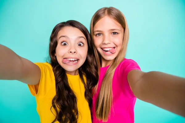 Foto de dos chicas casuales lindas que engañan felices mostrando lenguas a la cámara mientras se aíslan con fondo verde azulado — Foto de Stock