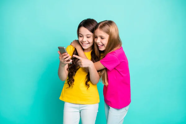 Foto de la moda alegre modelo agradable rubia morena novias vistiendo rosa y amarillo camisetas viendo algo divertido en el teléfono, mientras que aislado con fondo verde azulado —  Fotos de Stock