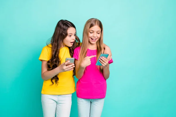 Photo de drôles occasionnels sympa mignon couple amical de petites amies brunes blondes portant des t-shirts jaunes roses se choquer avec quelque chose oh leurs téléphones tandis qu'isolé avec fond de sarcelle — Photo