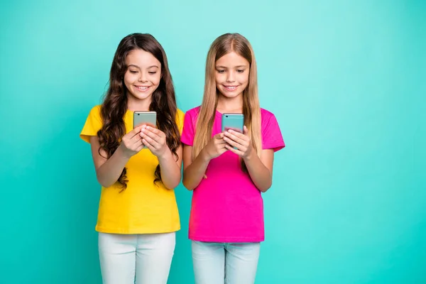 Foto de dos chicas navegando a través de sus teléfonos recién comprados escribiendo mensajes entre sí mientras están aisladas con fondo verde azulado —  Fotos de Stock