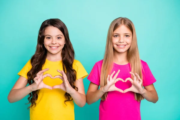 Foto de dois agradável bom tipo amigável meninas cabelos compridos vestindo amarelo e rosa t-shirts moldar corações com as mãos, enquanto isolado com fundo teal — Fotografia de Stock