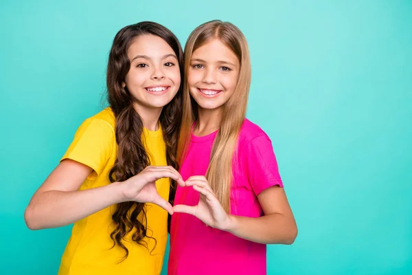 Foto de duas meninas abraçando moldar o coração com as mãos, enquanto isolado com fundo teal — Fotografia de Stock