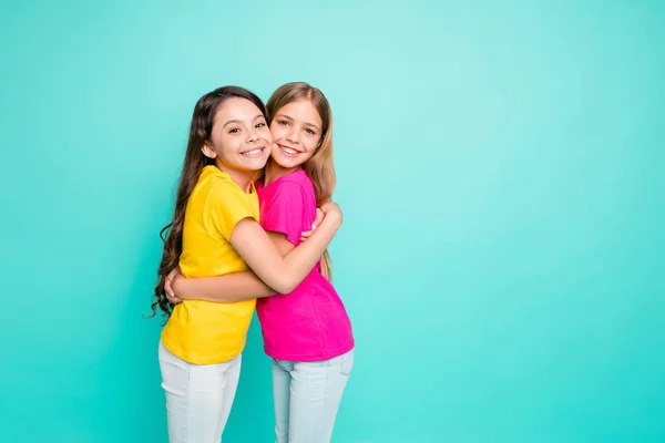 Foto de duas namoradas amigáveis bonitos tendo decidido abraçar um ao outro, enquanto isolado com fundo teal — Fotografia de Stock