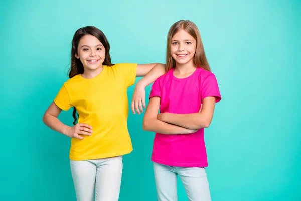 Foto de dos divertidas chicas lindas amigables blancas que usan camisetas amarillas y rosas mientras están aisladas con fondo verde azulado —  Fotos de Stock