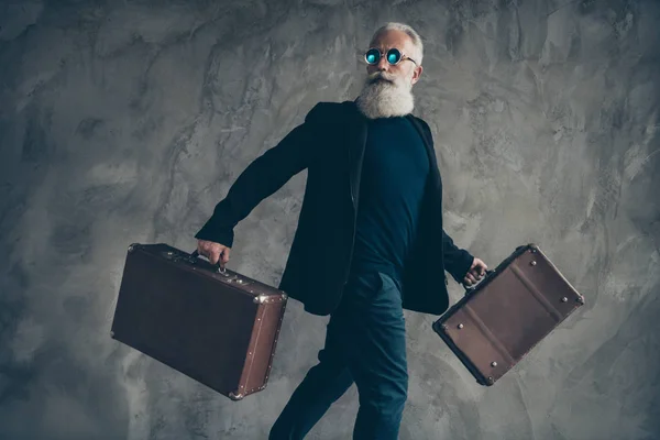 Retrato de hombre masculino duro fresco en gafas gafas llevar paquete anticuado desgaste pantalones impermeable negro aislado sobre fondo gris — Foto de Stock