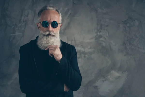 Retrato de un hombre masculino duro de mente tocándose la barbilla vistiendo impermeable negro aislado sobre fondo gris —  Fotos de Stock