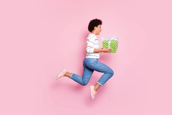 Πλήρες μήκος σώματος φωτογραφία της μόδας γλυκό τρελό εκστατικό δρομέα κρατώντας κουτί δώρου με τα χέρια της άλμα τρέξιμο για τις πωλήσεις σε τζιν ντένιμ πουλόβερ απομονωμένη Ροζ παστέλ χρώμα φόντο — Φωτογραφία Αρχείου