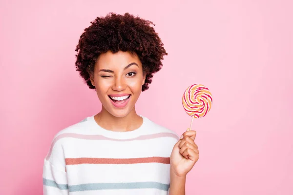 Photo of cheerful cute nice charming sweet girl holding candy with hands wearing white striped sweater blinking isolated over pastel color background — Stock Photo, Image