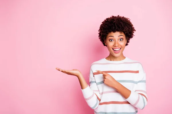 Foto de pele muito escura senhora ondulada indicando dedo na palma aberta aconselhando novo produto barato incrível desgaste listrado pulôver isolado pastel cor rosa fundo — Fotografia de Stock