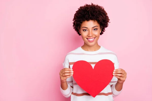 Foto de bonita señora de piel oscura sosteniendo en las manos gran corazón de papel rojo que expresa la seguridad cardíaca y el desgaste de la salud Jersey de rayas aislado pastel de color rosa de fondo —  Fotos de Stock