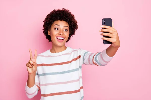 Foto de rizado lindo encantador alegre agradable joven tomando selfie que le muestra v-signo de usar suéter de rayas blancas aislado sobre fondo de color pastel rosa —  Fotos de Stock
