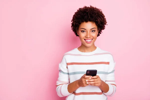 Zdjęcie z dość ciemnej skóry kręcone Lady trzymając telefon uzależniony od wypoczywać internetowych i komentarzy nosić białe paski na białym tle na odludziu pastel różowy tło — Zdjęcie stockowe