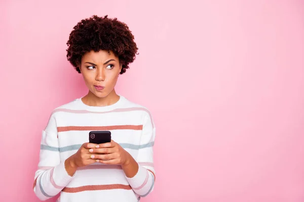 Foto de señora de piel bastante oscura sosteniendo teléfono dudoso sobre el nuevo instagram post desgaste blanco a rayas suéter aislado pastel rosa color fondo — Foto de Stock