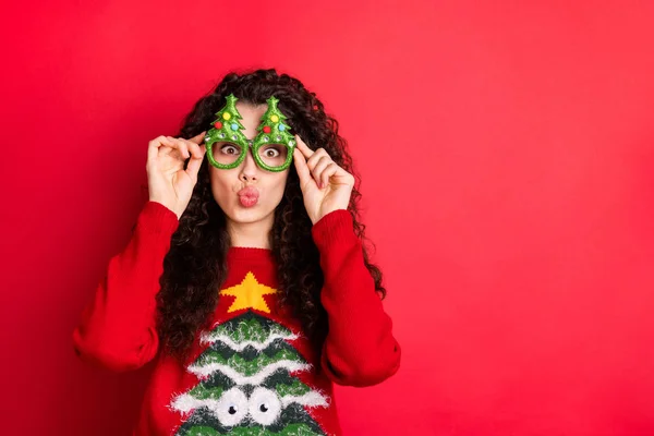 Fotó a vicces göndör hölgy küldő duzzogott csók játékos hangulat kopás funky örökzöld fák formában szemüveg kötött pulóver elszigetelt vörös színű háttér — Stock Fotó