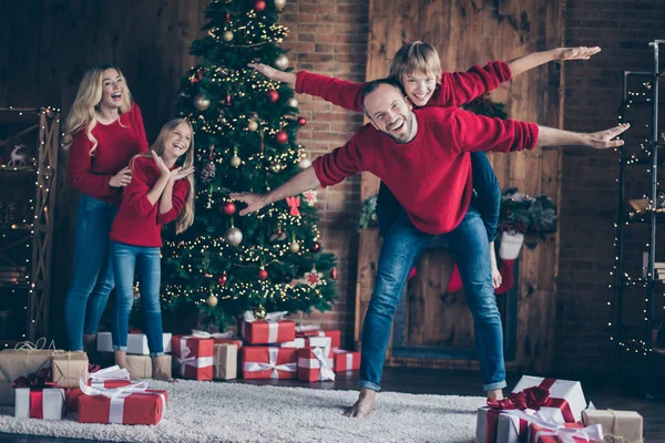 Полнометражное фото мамы и двух детей, проводящих рождественское утро вместе, изображающих воздушные полеты игры возле новогодней елки в красных свитерах — стоковое фото