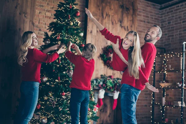 Foto do pai mãe e duas crianças passando x-mas manhã juntos fingindo voo de ar pendurado guirlandas bugigangas na árvore do ano novo dentro de casa usam camisolas vermelhas — Fotografia de Stock