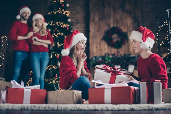 Profielfoto van volledige familie ouders kijken naar twee kinderen uitwisselen van x-mas geschenken zittend gezellige vloer in de buurt versierd Garland verlichting Nieuwjaar boom dragen Santa caps Red jumpers — Stockfoto