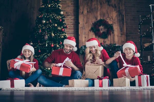 Foto de família grande perguntou pai mãe irmã irmão abertura x-mas presentes sentado chão perto de luzes de guirlanda decoradas árvore de ano novo dentro de casa desgaste Papai Noel caps pulôveres vermelhos — Fotografia de Stock