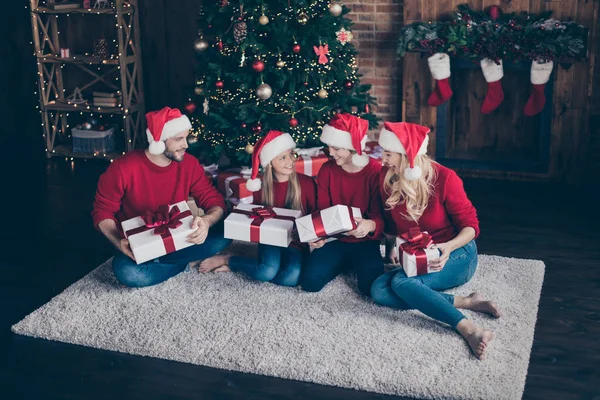 Uyum içinde tam aile fotoğrafı baba anne iki çocuk verilen x-mas hediyeler idika yakın zemin dekorasyonlu çelenk ışıkları yeni yıl ağacı kapalı santa caps ve kırmızı kazak giymek — Stok fotoğraf