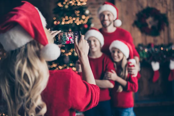 Foto borrada da mãe fazendo foto de duas crianças e pai perto da árvore decorada do ano novo guirlanda dentro de casa família x-mas atmosfera usar bonés de Papai Noel e camisolas vermelhas — Fotografia de Stock