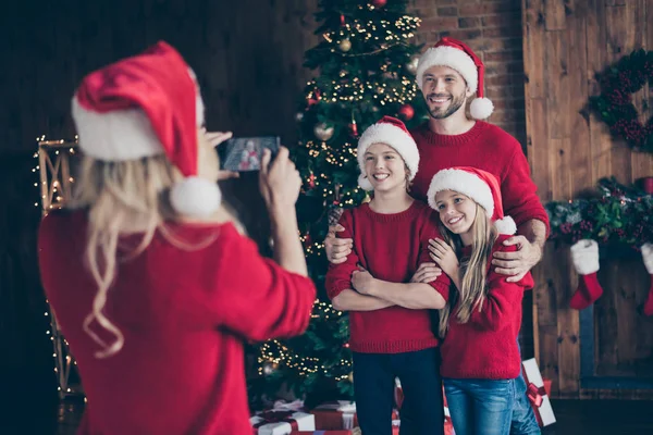 Photo de maman faisant la photo de deux enfants et papa près de guirlande décorée nouvel an arbre intérieur famille x-mas atmosphère porter santa casquettes et pulls rouges — Photo