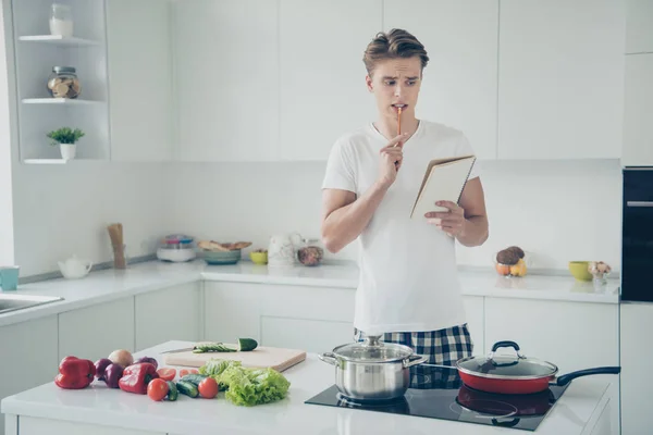 Retrato de su agradable chico confundido atractivo haciendo almuerzo escribiendo notas de lectura plan de compras la creación de una nueva receta en blanco claro estilo moderno interior de la casa en el interior — Foto de Stock