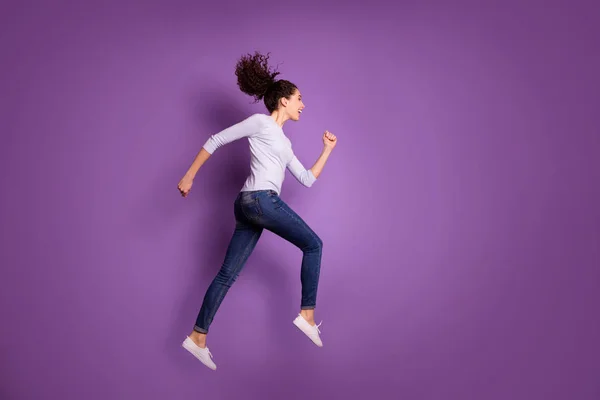 Volledige lengte lichaam grootte foto van vrolijke schattige charmante mooie sportieve vrouw dragen jeans denim sneakers running voor verkoop met haar geblazen gegooid springen geïsoleerd pastel kleur achtergrond — Stockfoto