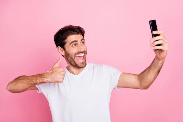 Retrato de divertido funky loco alegre Oriente Medio hombre blogger en las vacaciones de verano recomiendan sus vacaciones tomar selfie mostrar pulgar hacia arriba usar elegante camiseta blanca de moda aislado color rosa fondo — Foto de Stock