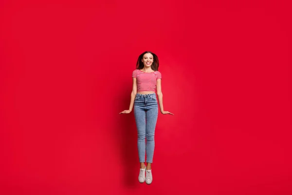 Kırmızı arka planda izole edilmiş kot pantolon giymeye hevesli sevimli, güzel bir kız arkadaşın vücut ölçülerinde tam boy fotoğrafı. — Stok fotoğraf