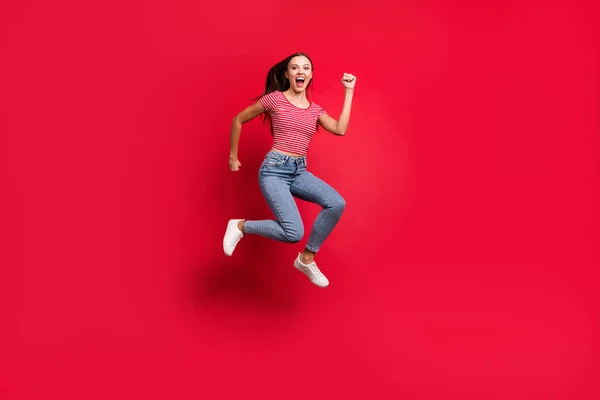 Повна довжина тіла модна фотографія божевільної переможниці дівчини в джинсах джинсового кольору різко біжить до торгового центру, ізольовано червоним тлом — стокове фото