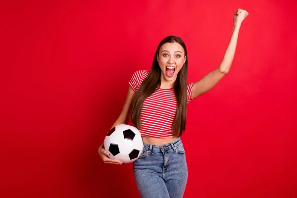 Fotografie roztomilé pěkné veselé vzrušené zábavné extatické přítelkyně přešťastný s vítězstvím svého týmu, zatímco izolované nad červeným pozadím drží míč s rukama nosí džíny džíny — Stock fotografie