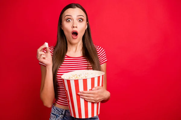 Photo of trendy scared brunette terrified girl eating pop corn wearing striped t-shirt watching horror movie while isolated with red background — Stock Photo, Image