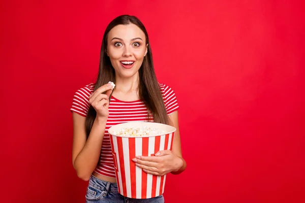 Foto van charmante mooie mooie mooie vriendin vroeg zich af met de smaak van popcorn dragen gestreept t-shirt terwijl geïsoleerd met rode achtergrond — Stockfoto