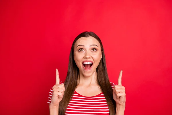 Фото очаровательной модной фанки смешно интересно чрезмерно радостный шокированный ступор девушка в полосатой футболке указывая на продажи со скидками в то время как изолированы на красном фоне — стоковое фото