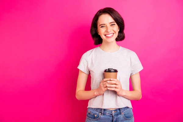 Фото чарівної милої чарівної привабливої дівчини, яка посміхається зубно тримає чашку кави в джинсах, ізольованої на рожевому яскравому кольоровому фоні — стокове фото