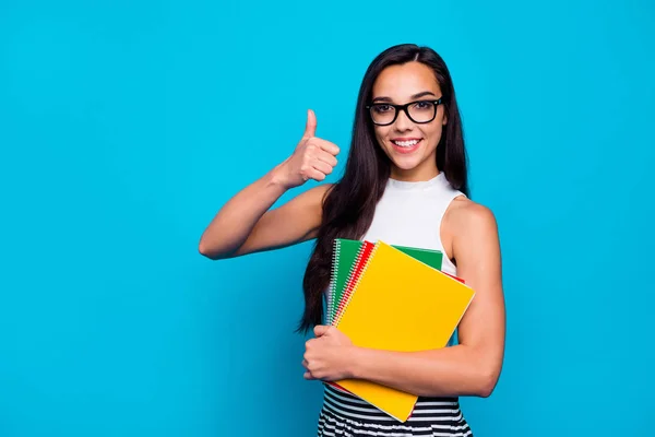 Fotografie hezké dámy drží studijní knihu v náručí pilný student zvedání palec nahoru oblečení specifikace bílá tank-top a pruhované sukně izolované modré barvy pozadí — Stock fotografie