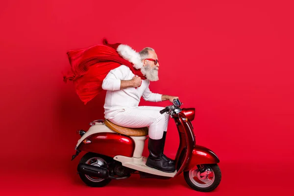Profile side view of nice bearded gray-haired Saint Nicholas riding motor delivering carrying desirable purchase things December wintertime isolated on bright vivid shine red background — Stock Photo, Image