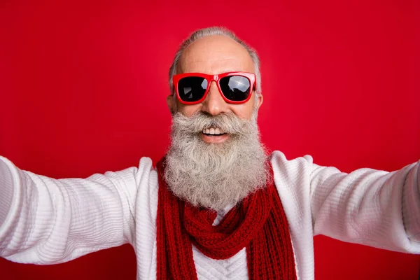 ชายซานต้าผู้สูงอายุที่ตื่นเต้น กําลังถ่ายรูปตัวเอง ใส่ชุดกันแดด กระโดดถักพื้นหลังสีแดง — ภาพถ่ายสต็อก